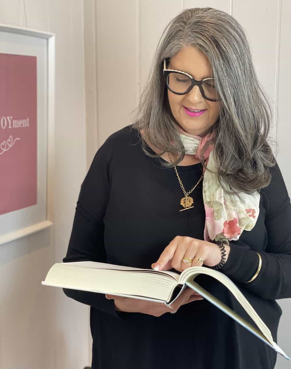 A woman holding a book in front of a wall.