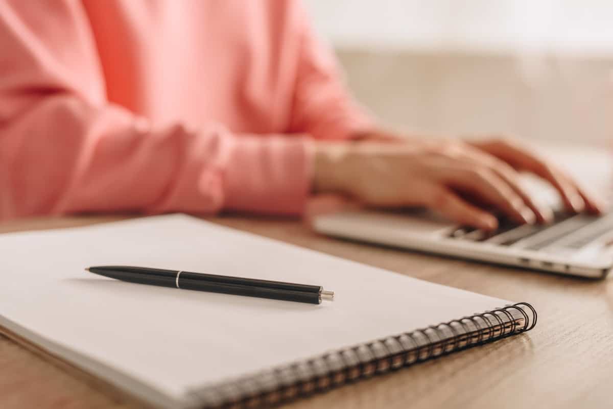 A woman typing on a laptop while holding a pen.