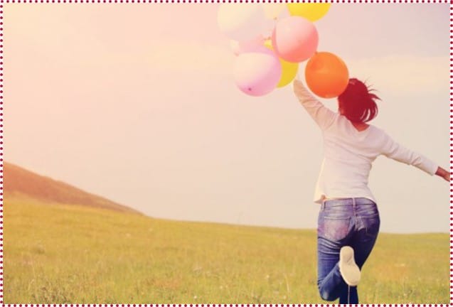 A woman is joyfully running through a field, holding colorful balloons.